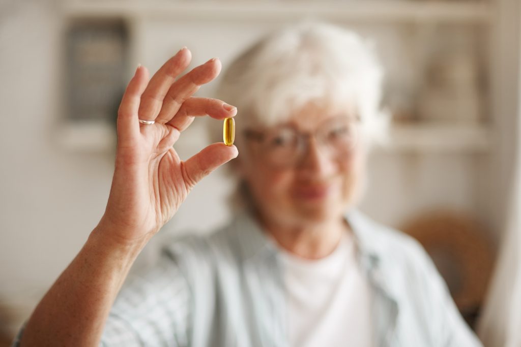 concepto alimentacion nutricion dieta salud primer plano mano anciana aceite pescado o suplemento acidos grasos poliinsaturados omega 3 forma capsula que tomar almuerzo